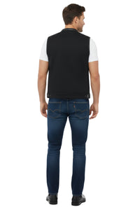Man wearing a black vest over a white shirt and blue jeans on a white background