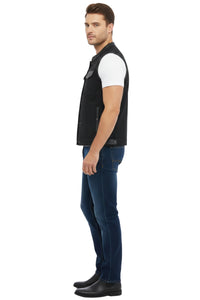 Man wearing a black vest over a white shirt with dark jeans on a white background