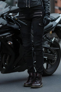 Person wearing black motorcycle gear standing next to a black motorcycle.