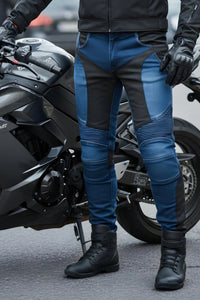Person wearing blue and black motorcycle pants standing next to a motorcycle.
