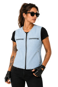 A woman modeling a light blue denim motorcycle vest over a black t-shirt, paired with black pants, black leather fingerless gloves, and sunglasses, against a solid white background.