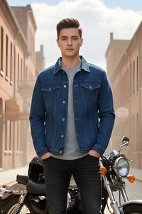 Man wearing a blue denim jacket standing next to a motorcycle on a street.