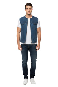 Man wearing a blue denim vest over a white shirt with dark jeans on a white background