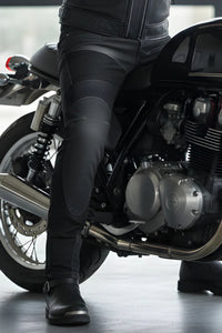 Person wearing black leather pants and shoes sitting on a motorcycle.