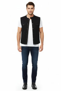 Man wearing a black vest over a white shirt with dark jeans on a white background