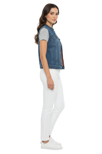 Woman wearing a denim vest over a gray shirt with white pants on a white background